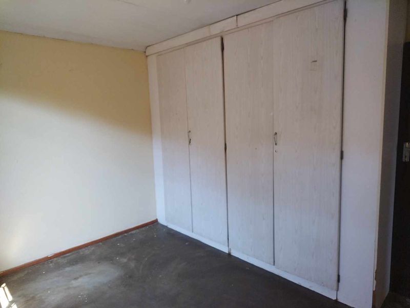 A vacant bedroom featuring built-in cupboards with a dated finish, requiring cosmetic updates to the flooring and wall surfaces.
