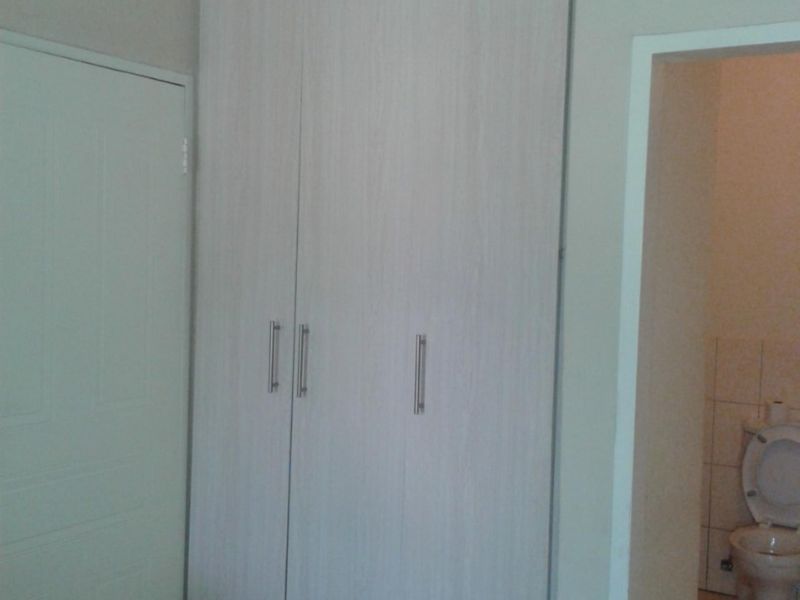 A bedroom featuring built-in cupboards with light wood-grain finish and tiled flooring, with an adjacent view into a tiled bathroom.