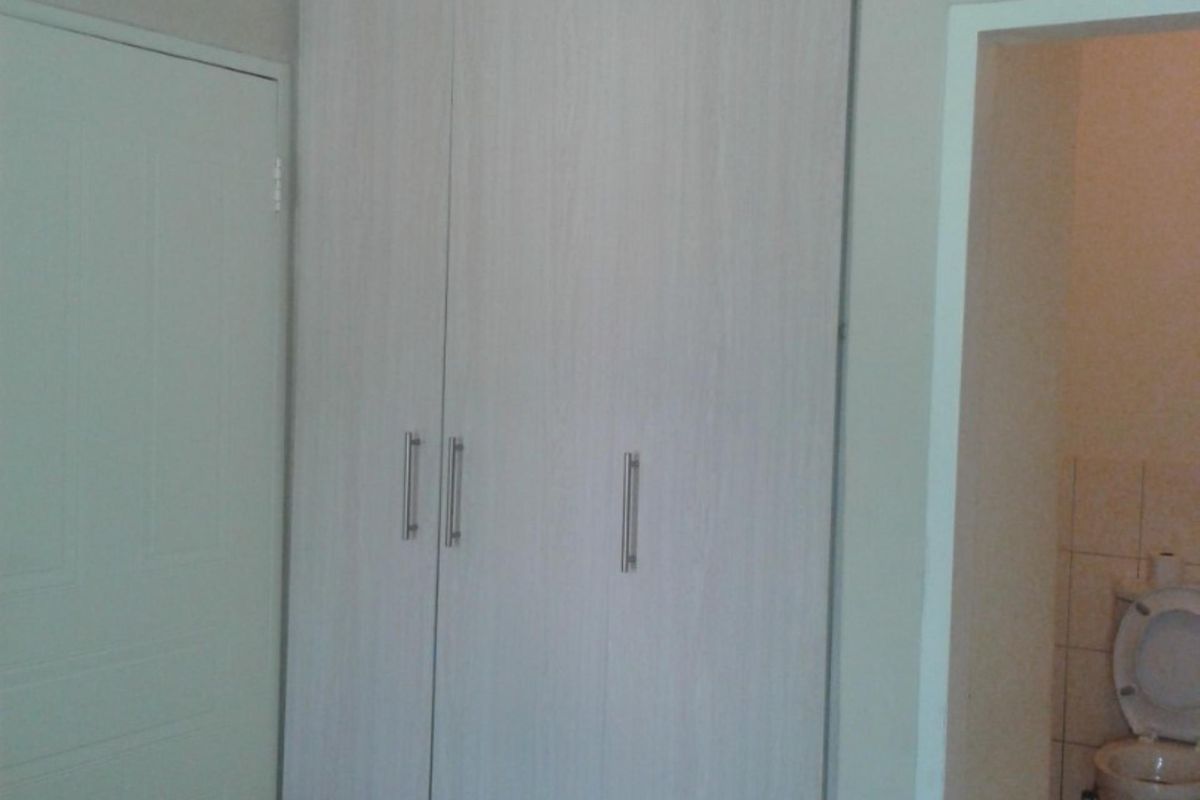 A bedroom featuring built-in cupboards with light wood-grain finish and tiled flooring, with an adjacent view into a tiled bathroom.