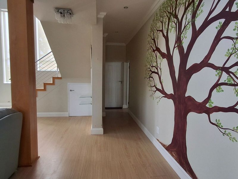 A bright hallway featuring laminate flooring, a staircase with modern railings, and a decorative wall mural, leading towards a secondary interior door.