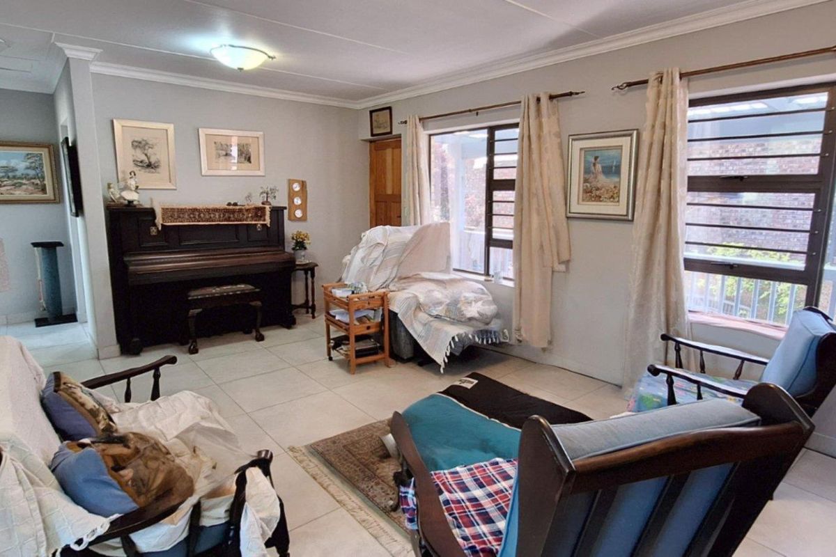 A spacious living room featuring tiled flooring, large windows with security bars, and crown molding, offering a bright and functional living space.