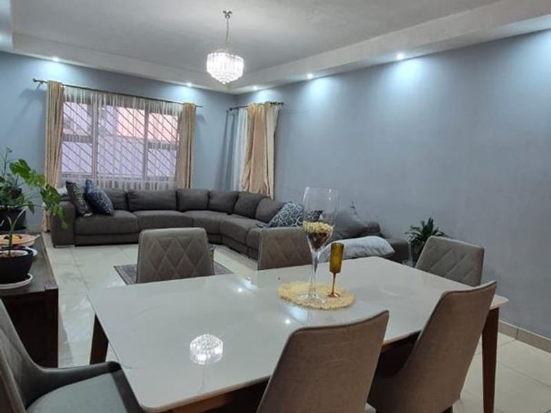 An open-plan living and dining area featuring tiled flooring, recessed downlighting, and a central crystal chandelier, creating a bright and functional living space.