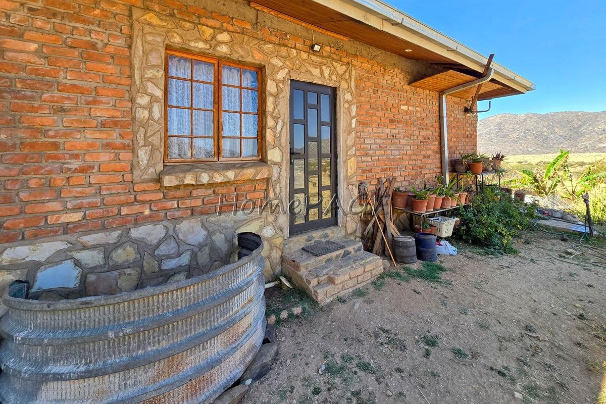 Rear exterior view of a rustic brick and stone cottage featuring timber-framed windows and a corrugated metal water tank in a rural setting.