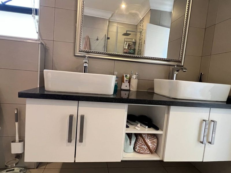 A modern bathroom featuring a double vanity with vessel sinks, chrome faucets, a wall-mounted toilet, and neutral wall tiling.