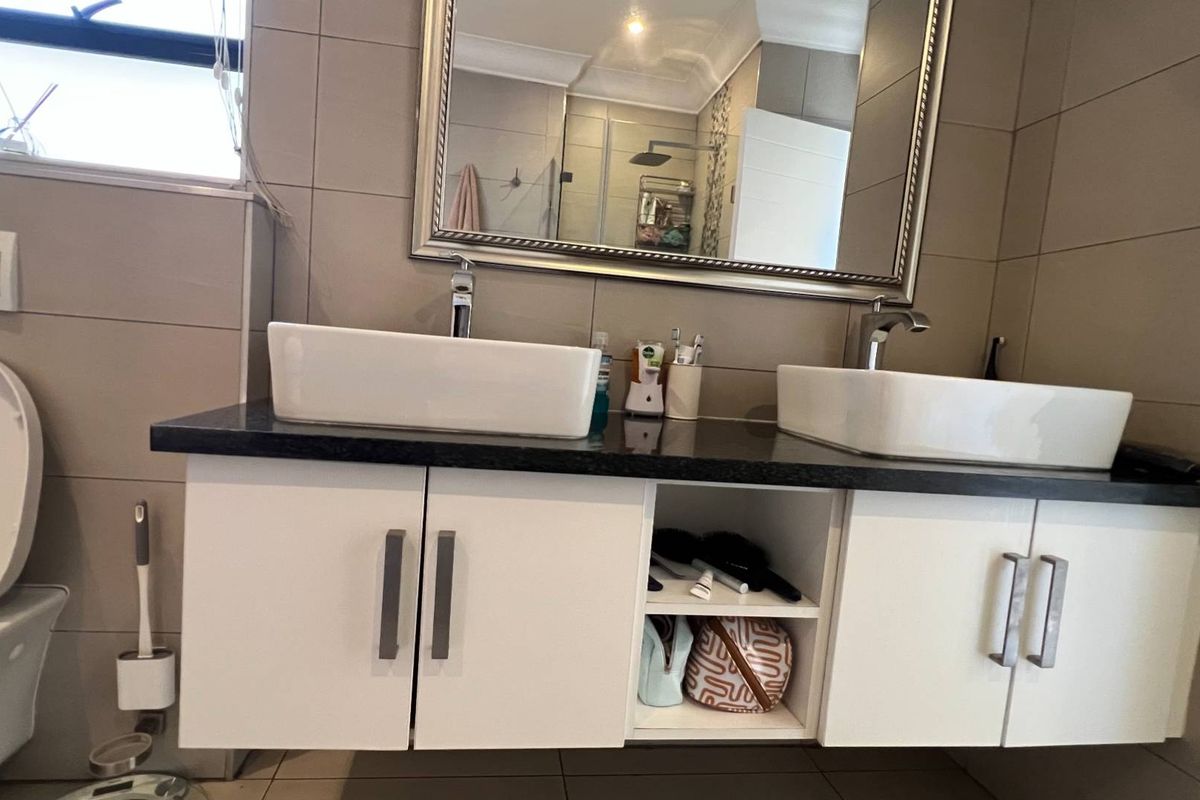 A modern bathroom featuring a double vanity with vessel sinks, chrome faucets, a wall-mounted toilet, and neutral wall tiling.