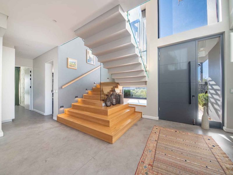 Modern entrance hall featuring a striking floating timber staircase with glass balustrade, polished concrete floors, and a large contemporary pivot front door.