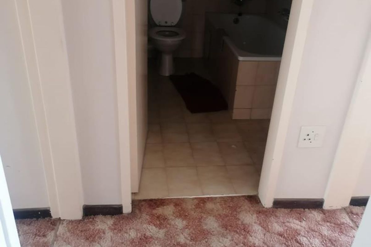 A dated bathroom featuring a standard bathtub and toilet, accessible from a carpeted hallway area.