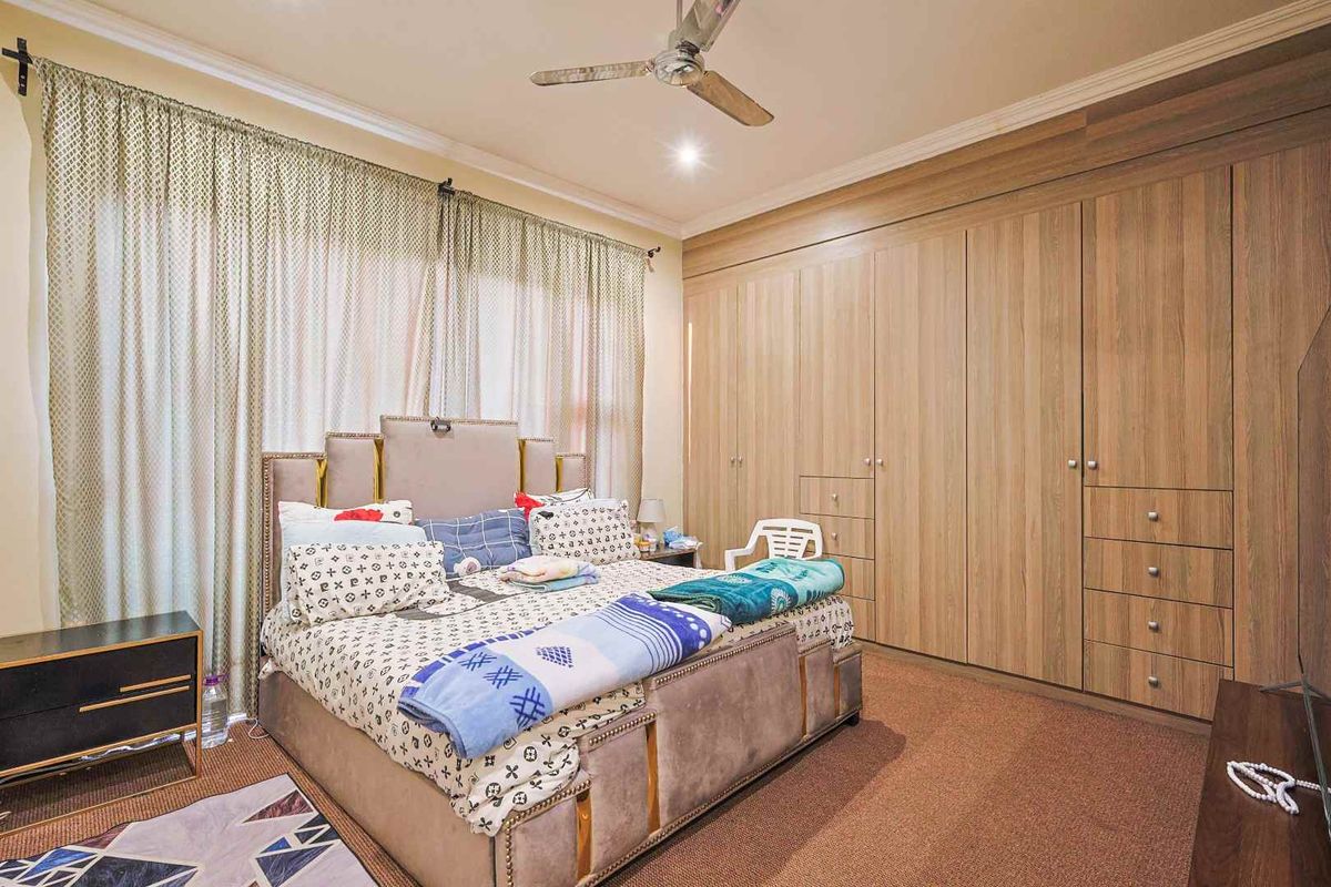 A well-maintained bedroom featuring extensive floor-to-ceiling built-in wooden cupboards, neutral carpeting, and a functional ceiling fan.