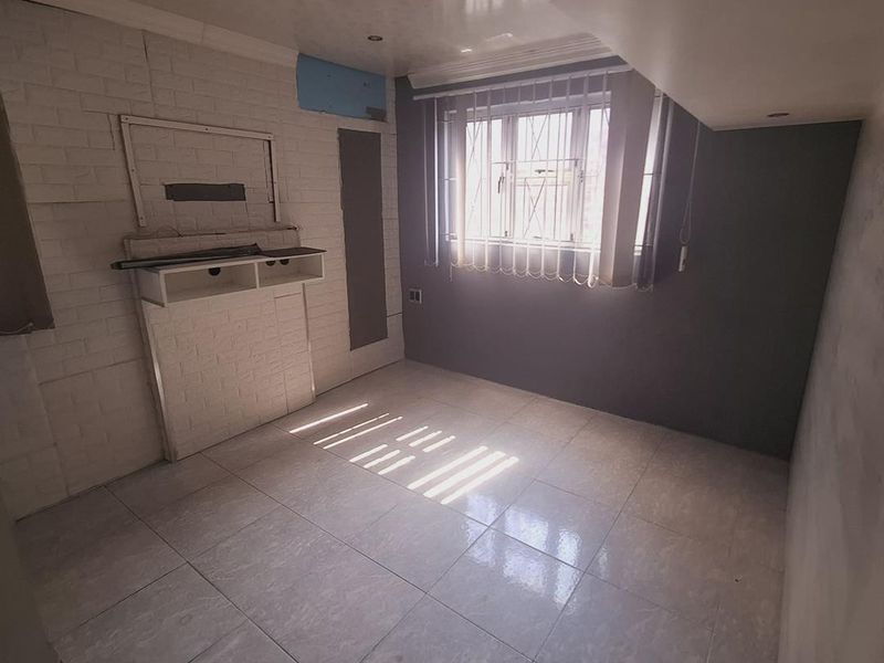 An empty bedroom featuring tiled flooring, a built-in shelving unit, and security bars on the window, requiring minor cosmetic finishing to the walls.