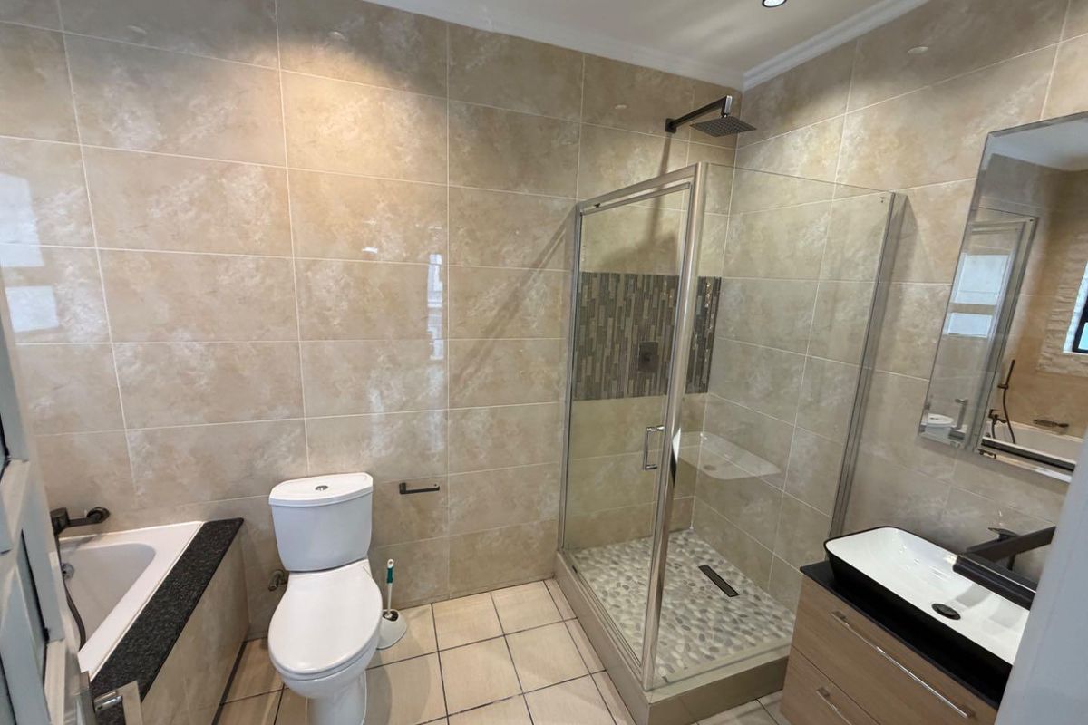 Modern bathroom featuring a walk-in shower with pebble floor, built-in bathtub, vanity with vessel sink, and neutral wall tiling.