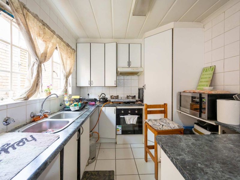 A compact, dated kitchen featuring white cabinetry, a double basin sink, built-in oven with gas hob, and tiled splashbacks.