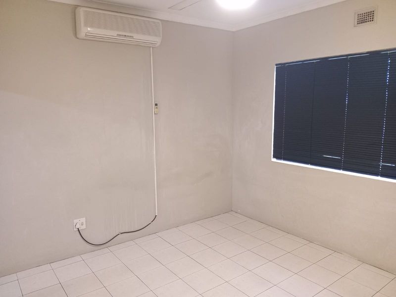 An empty bedroom featuring tiled flooring, a wall-mounted split-system air conditioner, and dark venetian blinds.