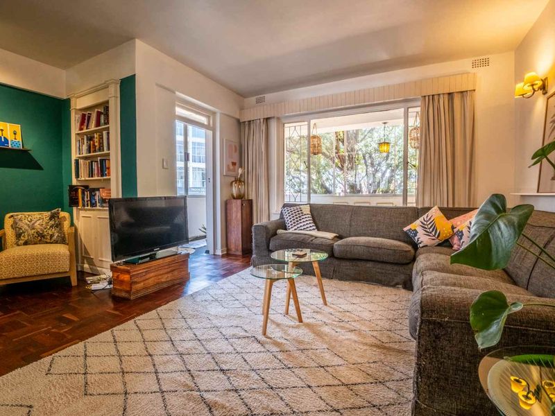 A well-lit living room featuring classic parquet flooring, built-in shelving, and large windows that provide natural light and access to an outdoor balcony area.
