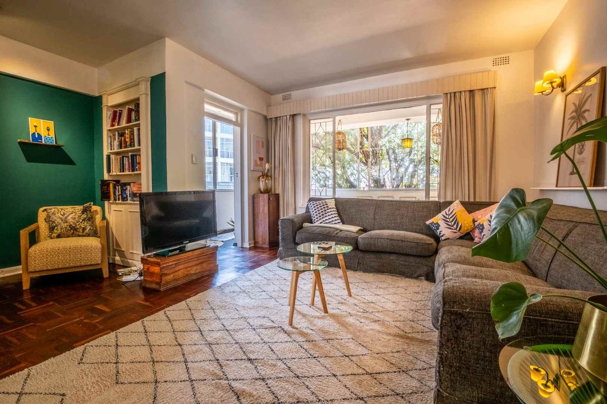 A well-lit living room featuring classic parquet flooring, built-in shelving, and large windows that provide natural light and access to an outdoor balcony area.