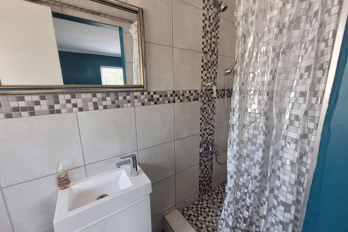A compact bathroom featuring a wall-mounted vanity with basin, tiled walls with mosaic accents, and a shower area with a mixer and shower head.