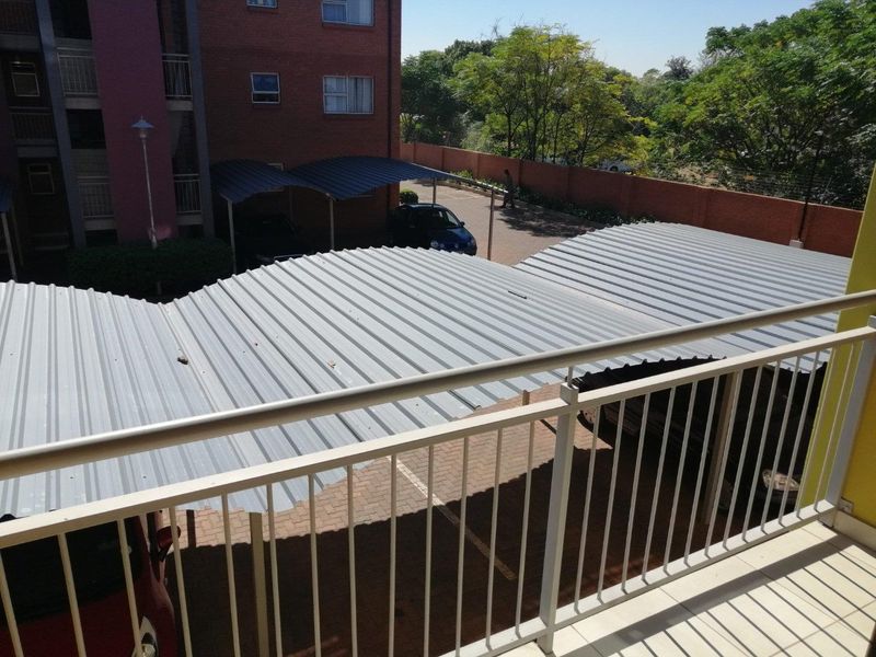 A view from a balcony overlooking the apartment complex parking area with covered carports and brick boundary walls.