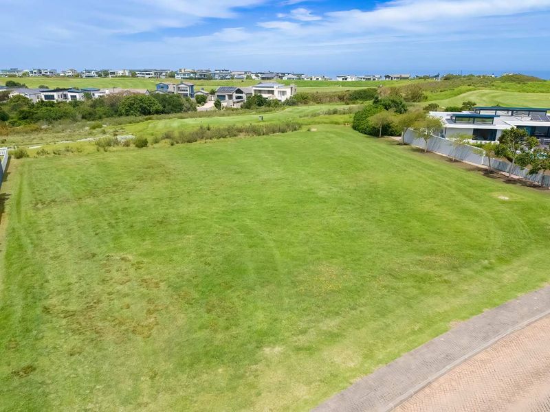 An aerial view of a vacant residential plot featuring a well-maintained grass lawn, situated in a developed estate with surrounding homes.