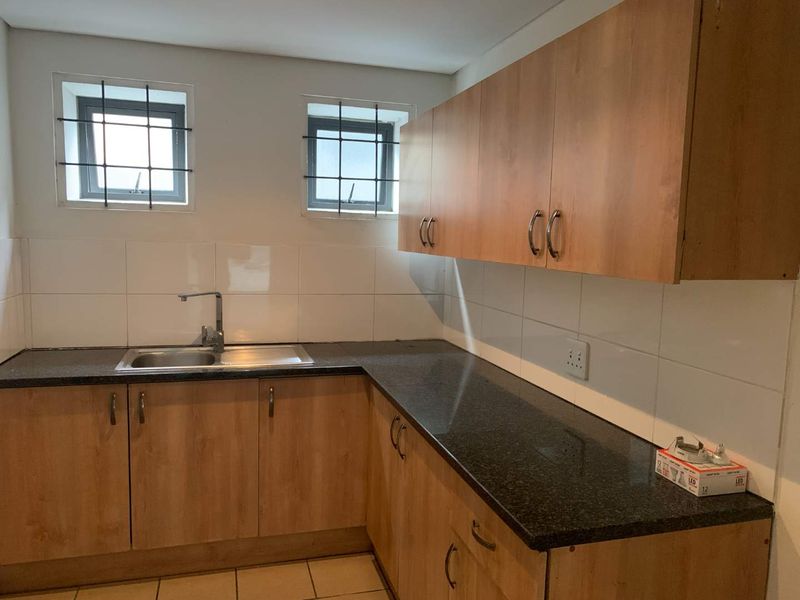 A functional kitchen area featuring laminate cabinetry, granite countertops, a stainless steel sink, and tiled backsplash with security-fitted windows.