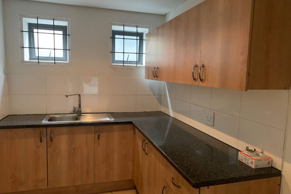 A functional kitchen area featuring laminate cabinetry, granite countertops, a stainless steel sink, and tiled backsplash with security-fitted windows.
