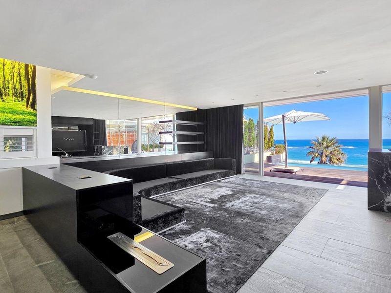 Modern living room featuring sleek built-in fireplace, recessed lighting, and expansive sliding glass doors opening to a scenic ocean view and pool deck.