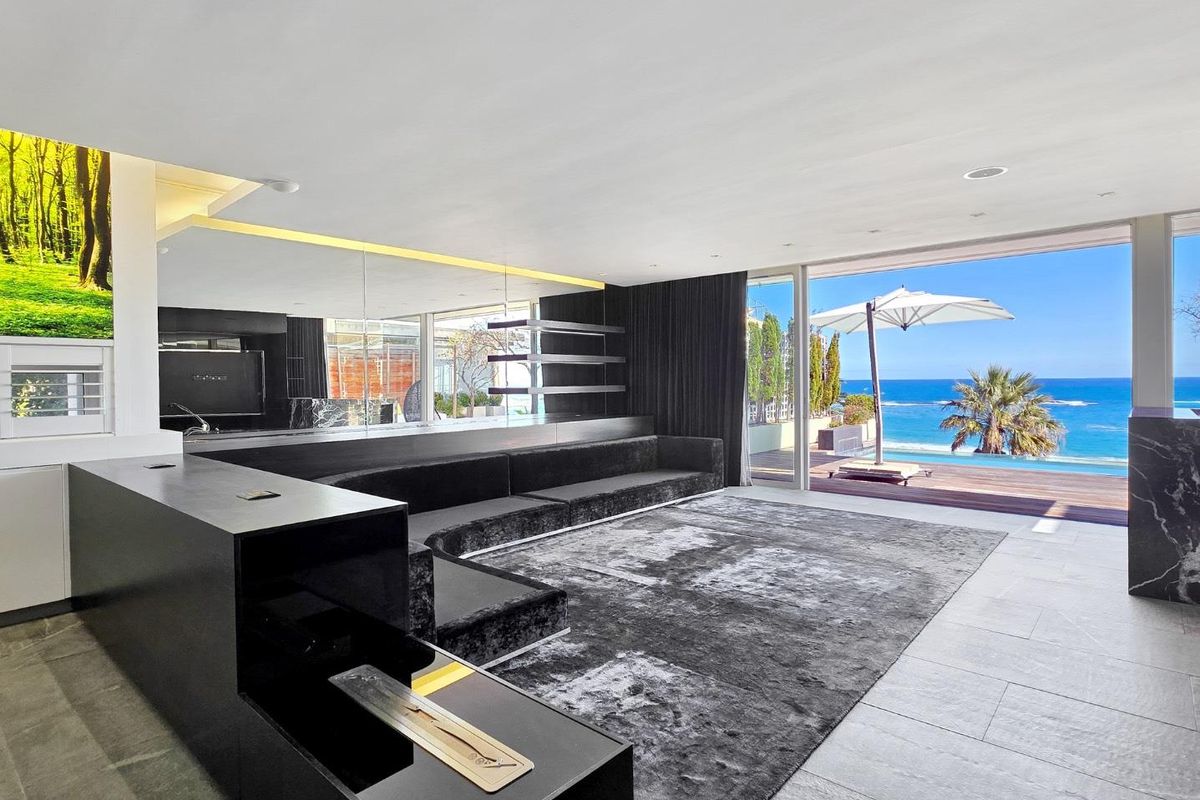 Modern living room featuring sleek built-in fireplace, recessed lighting, and expansive sliding glass doors opening to a scenic ocean view and pool deck.