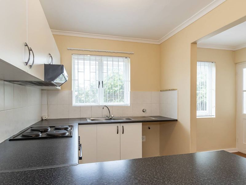 A functional kitchen featuring built-in cabinetry, dark laminate countertops, an electric hob with extractor fan, and a stainless steel sink with tiled splashback.