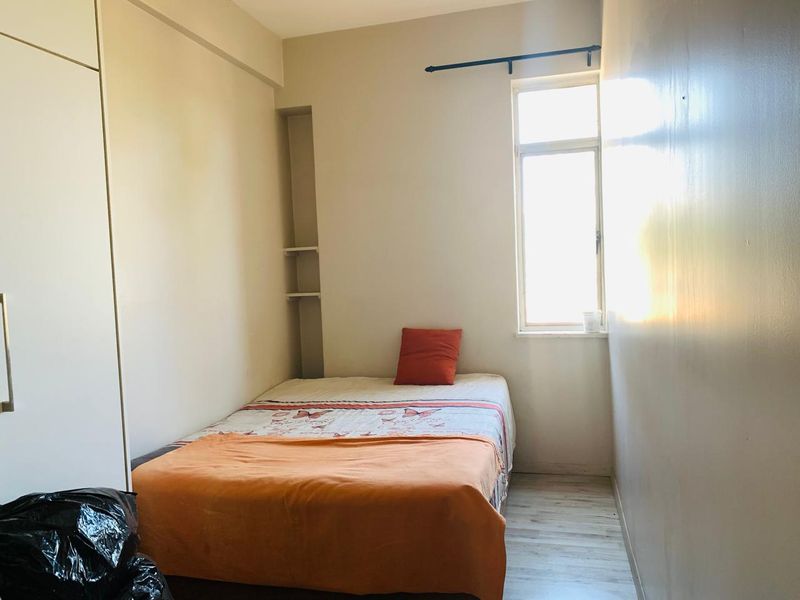 A compact bedroom featuring built-in wardrobe storage, recessed wall shelving, and light-toned laminate flooring, offering a functional space with natural light.