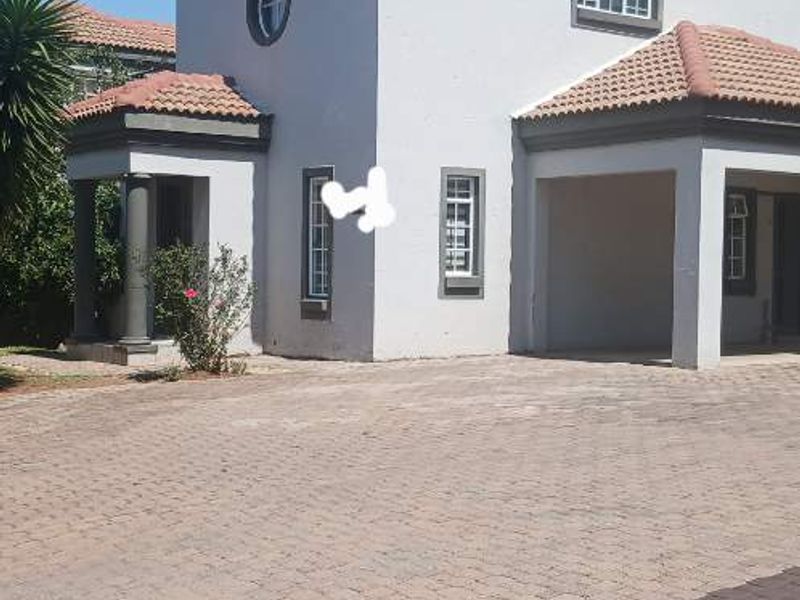 Front elevation of a townhouse featuring a paved driveway, covered entrance with decorative columns, and a tiled roof.