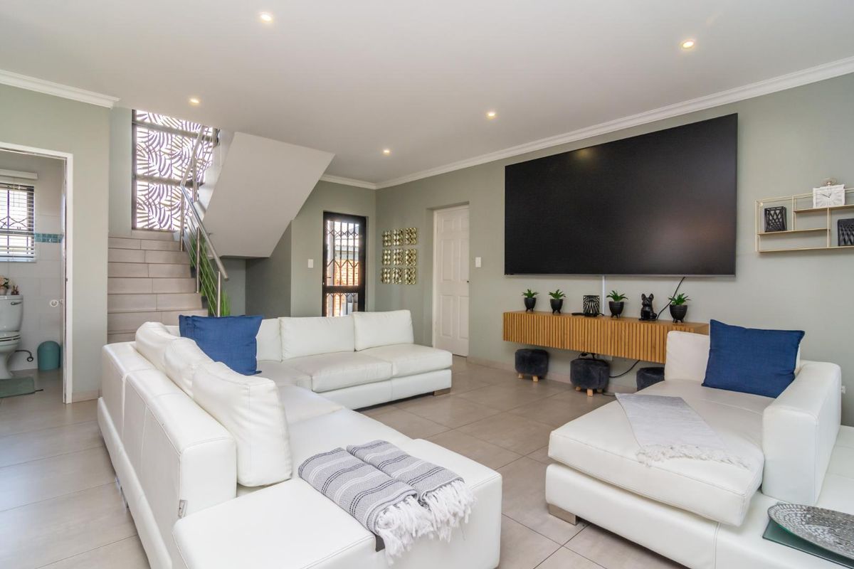 Spacious living room featuring tiled flooring, recessed lighting, and a staircase with decorative metal screen detailing.