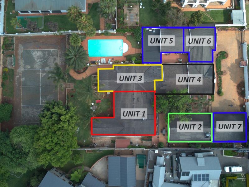 Aerial view of a residential property complex featuring multiple units, a swimming pool, and a tennis court set within a landscaped garden.