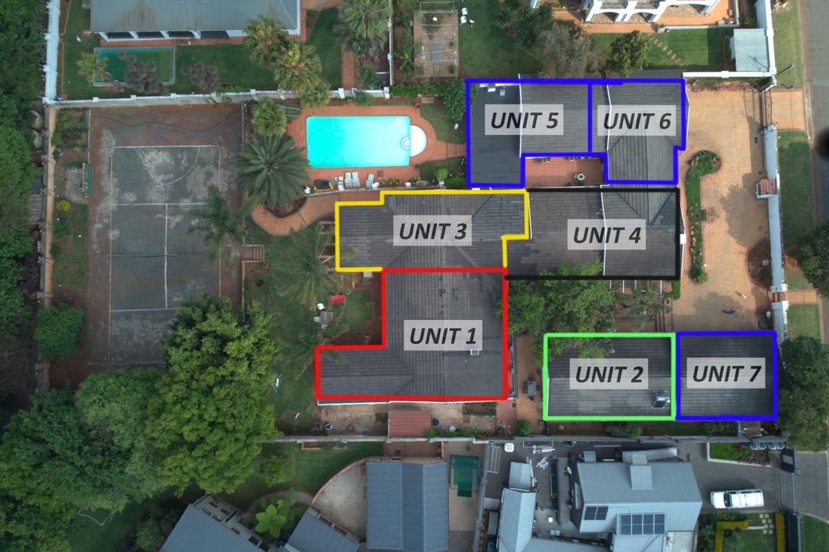 Aerial view of a residential property complex featuring multiple units, a swimming pool, and a tennis court set within a landscaped garden.