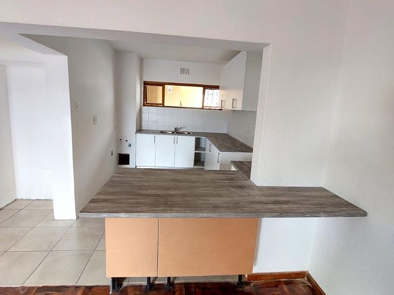 Open plan kitchen and living area featuring parquet flooring, white cabinetry, and a breakfast bar counter, currently in need of finishing touches.