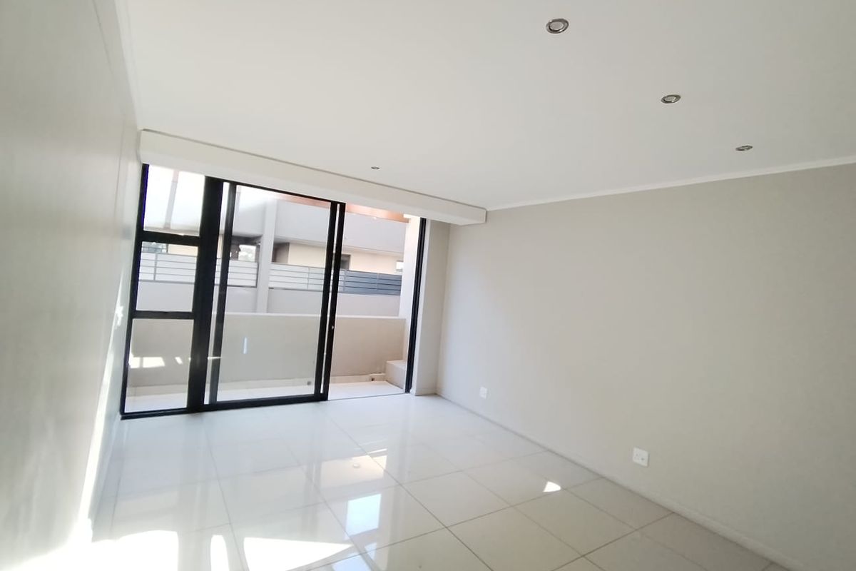 A bright, empty living area featuring polished tile flooring, recessed lighting, and large sliding glass doors leading to an outdoor balcony space.