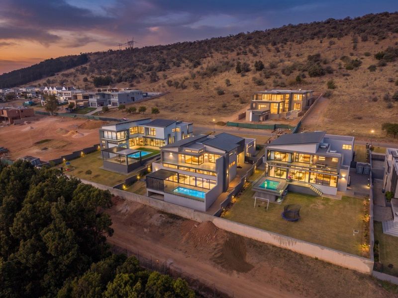 Aerial view of a modern residential estate featuring contemporary multi-story homes with private swimming pools, landscaped gardens, and expansive outdoor patio areas at dusk.