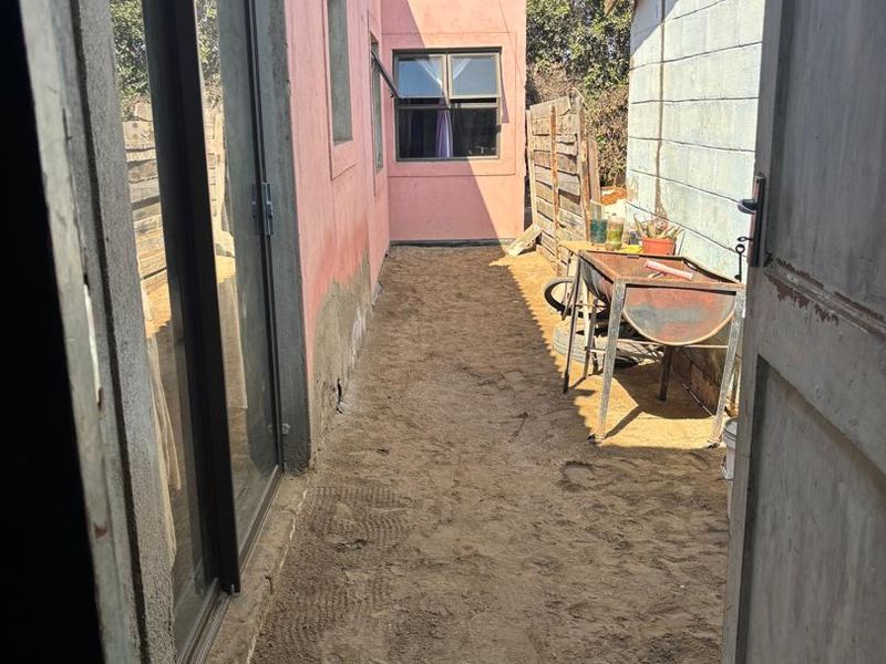 A narrow rear exterior passage featuring a sliding glass door, concrete block wall, and unpaved ground area requiring landscaping or paving.