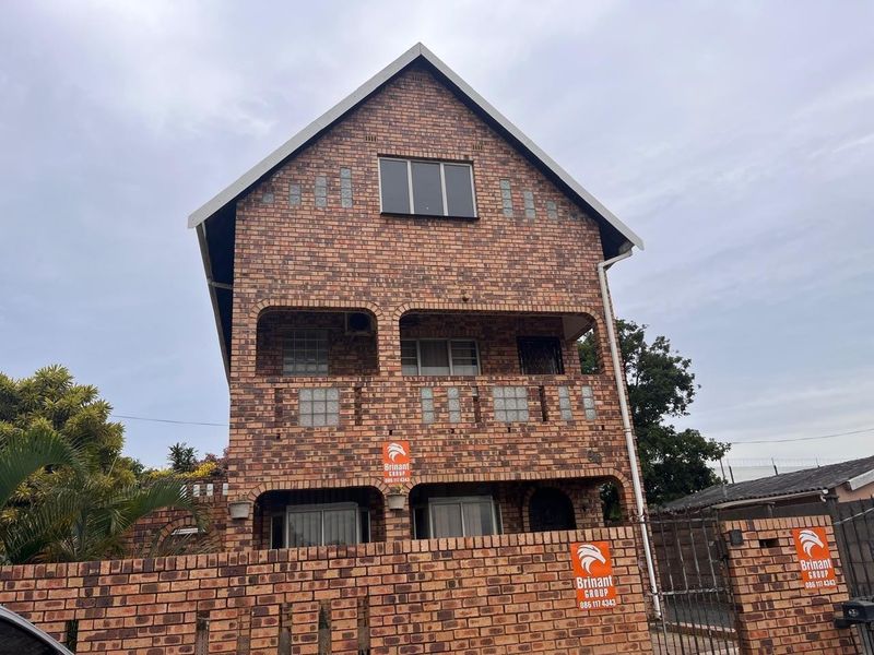 A multi-story face brick residential property featuring a gabled roof, integrated balconies, and a matching brick boundary wall.