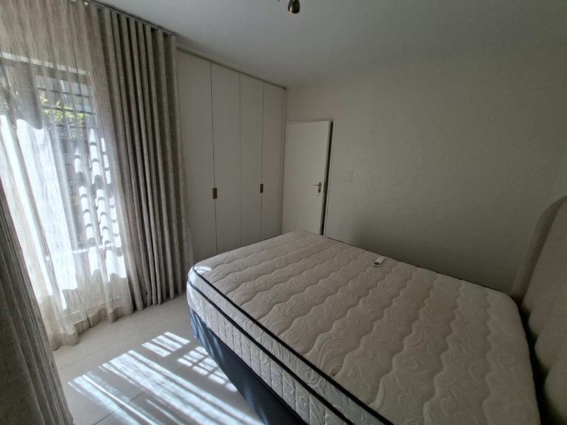 A well-lit bedroom featuring neutral tiled flooring, floor-to-ceiling curtains, and ample built-in cupboard storage space.
