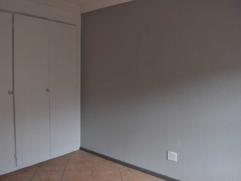 A simple bedroom featuring tiled flooring, a built-in wardrobe, and neutral grey walls, providing a clean and functional space.