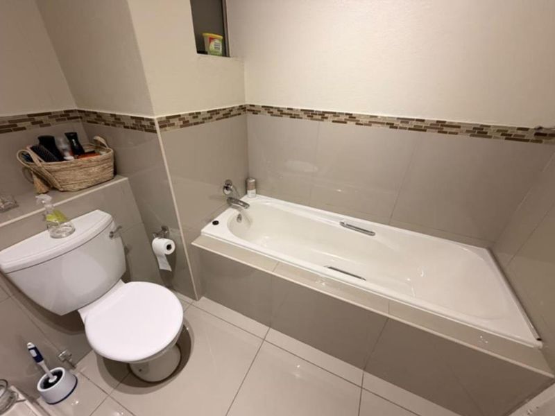 A clean, functional bathroom featuring a built-in bathtub, toilet, and neutral tiled finishes with a decorative mosaic border.