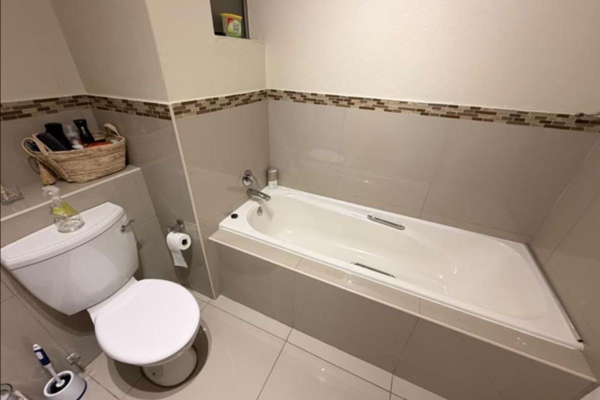 A clean, functional bathroom featuring a built-in bathtub, toilet, and neutral tiled finishes with a decorative mosaic border.