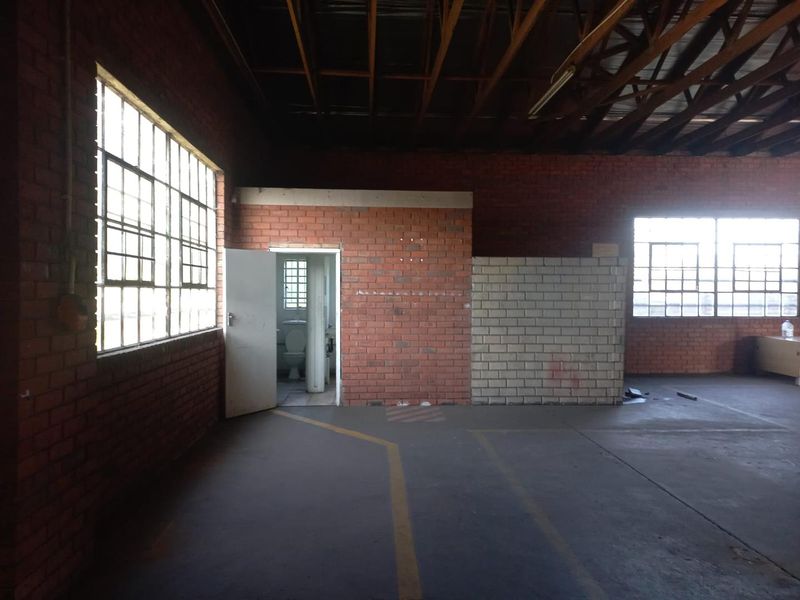 Spacious industrial utility area featuring exposed brick walls, high timber truss ceilings, large steel-framed windows, and an integrated internal restroom facility.