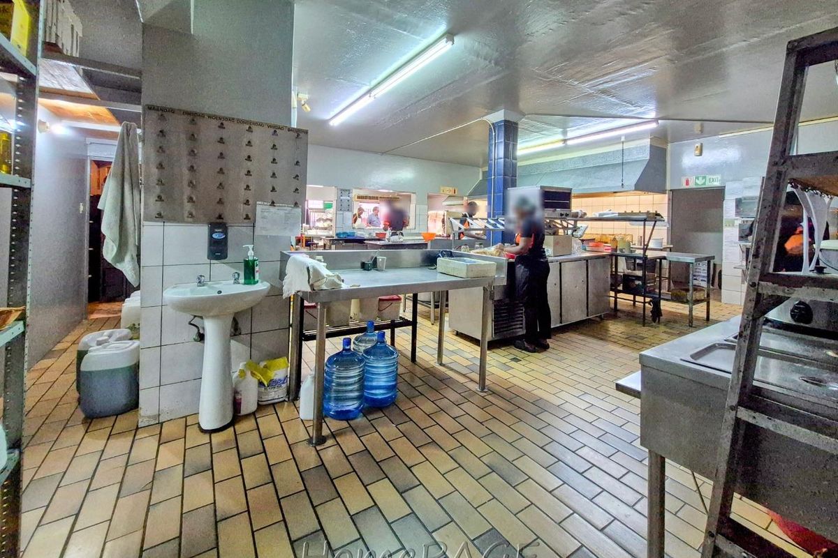 A functional commercial kitchen featuring tiled flooring, stainless steel prep stations, a wall-mounted basin, and integrated ventilation systems for professional food preparation.
