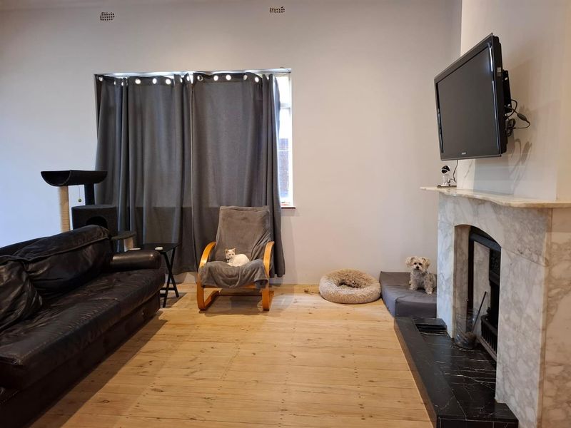 Living room featuring a classic marble fireplace, wall-mounted television, and exposed timber flooring.