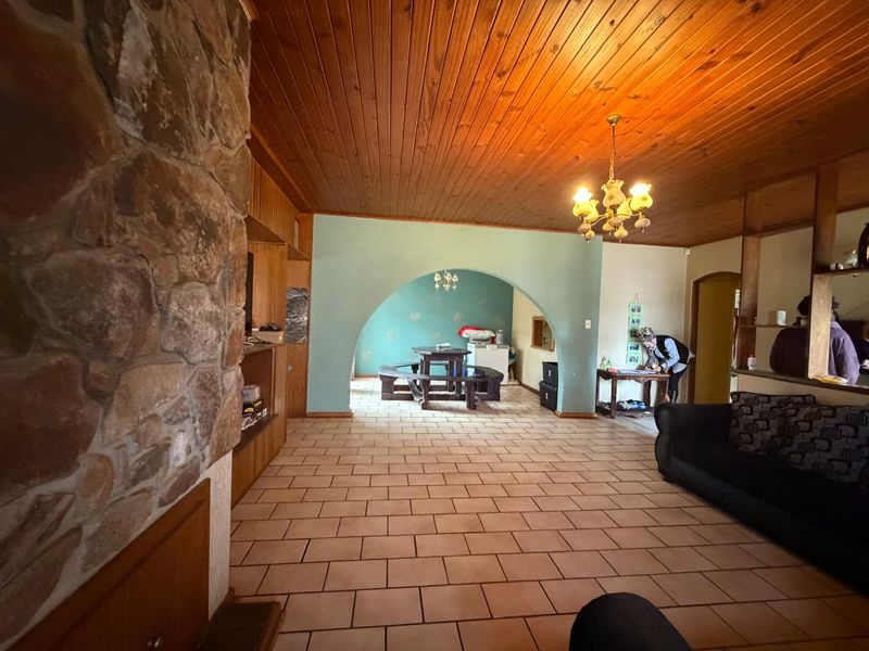 Open plan living area featuring a stone fireplace, timber ceiling, and tiled flooring with a distinct architectural archway connecting to the adjacent space.
