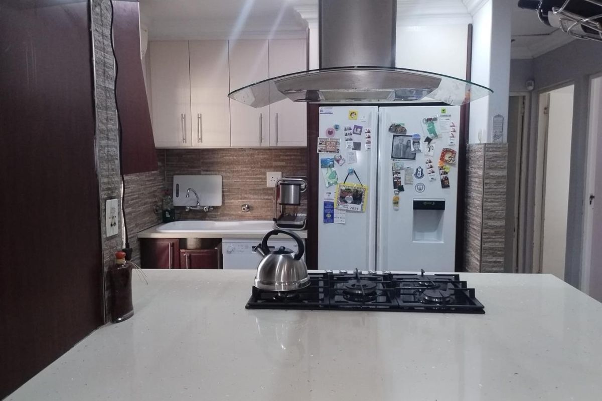 A functional kitchen featuring a central island with a gas hob, extractor fan, stone countertops, and ample built-in cabinetry.