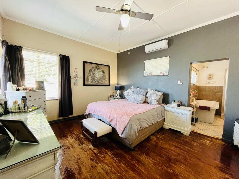 Spacious bedroom featuring polished timber flooring, a ceiling fan, and an integrated air conditioning unit, with direct access to an en-suite bathroom.