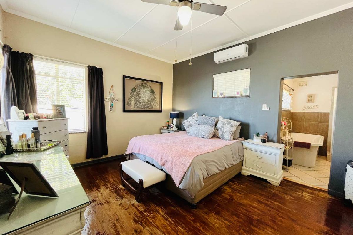 Spacious bedroom featuring polished timber flooring, a ceiling fan, and an integrated air conditioning unit, with direct access to an en-suite bathroom.
