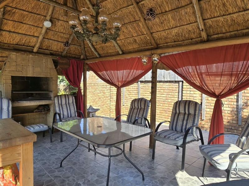 Covered outdoor patio area featuring a traditional thatched roof, built-in braai, and tiled flooring, ideal for relaxed outdoor entertaining.