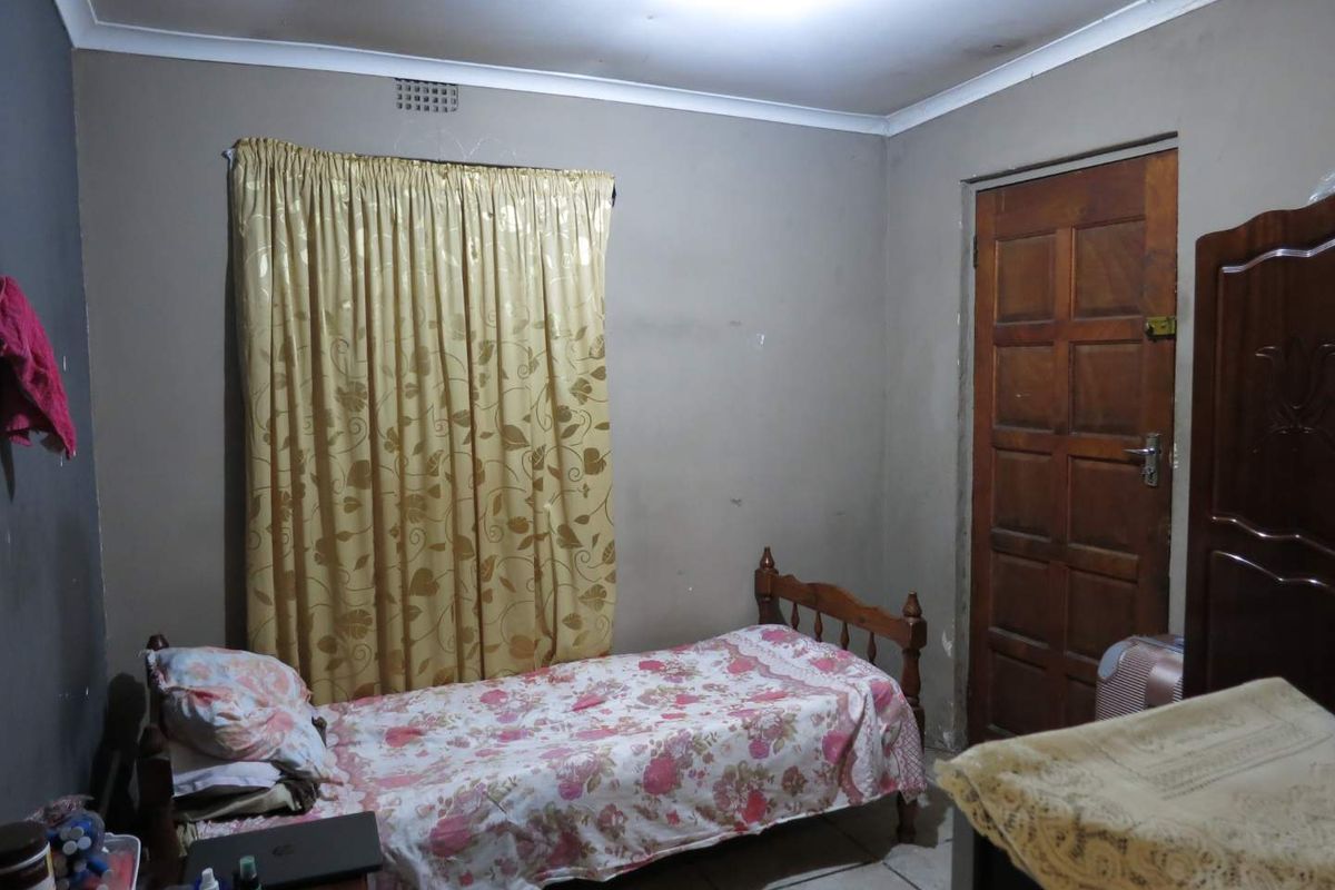 A functional bedroom featuring tiled flooring, a wooden door, and a window with curtain fixtures.