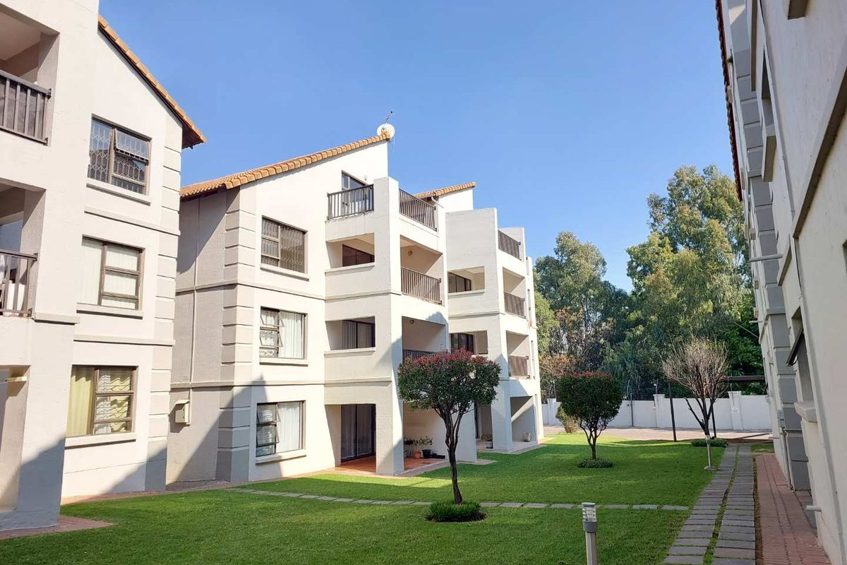 Exterior view of a multi-story apartment complex featuring private balconies, well-maintained green lawns, and paved walkways within a secure residential estate.